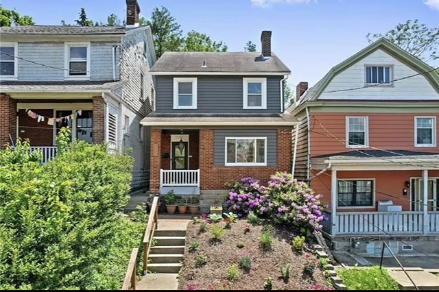 Charming gray and brick two-story home with blooming rhododendrons listed for sale in Pittsburgh