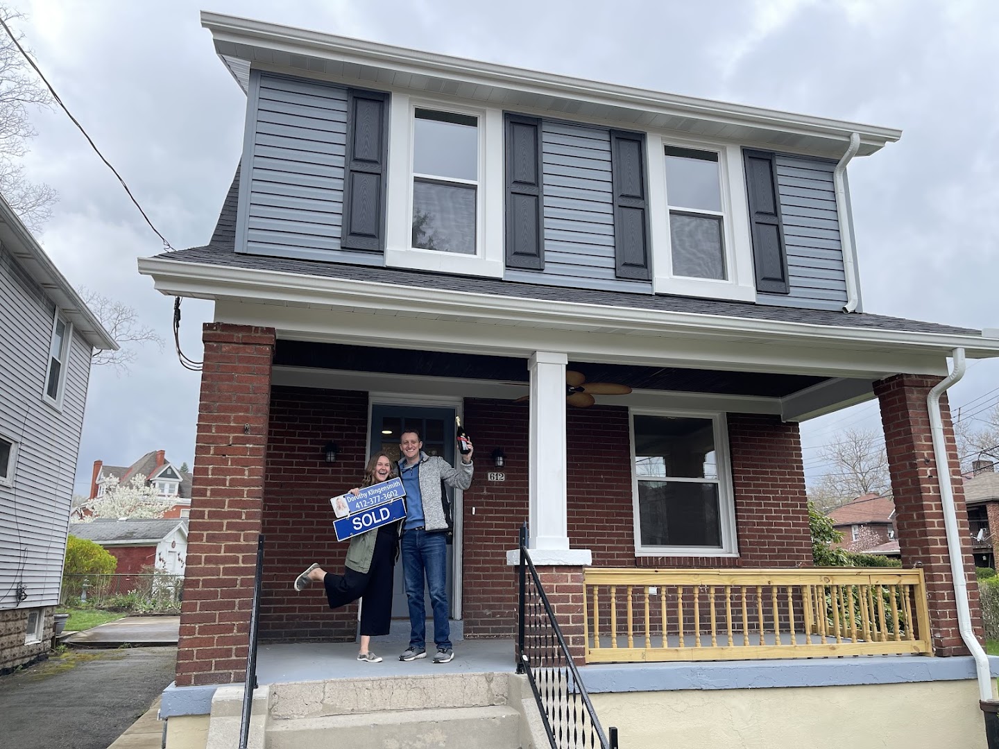 Happy couple celebrating with SOLD sign outside a renovated brick Pittsburgh home
