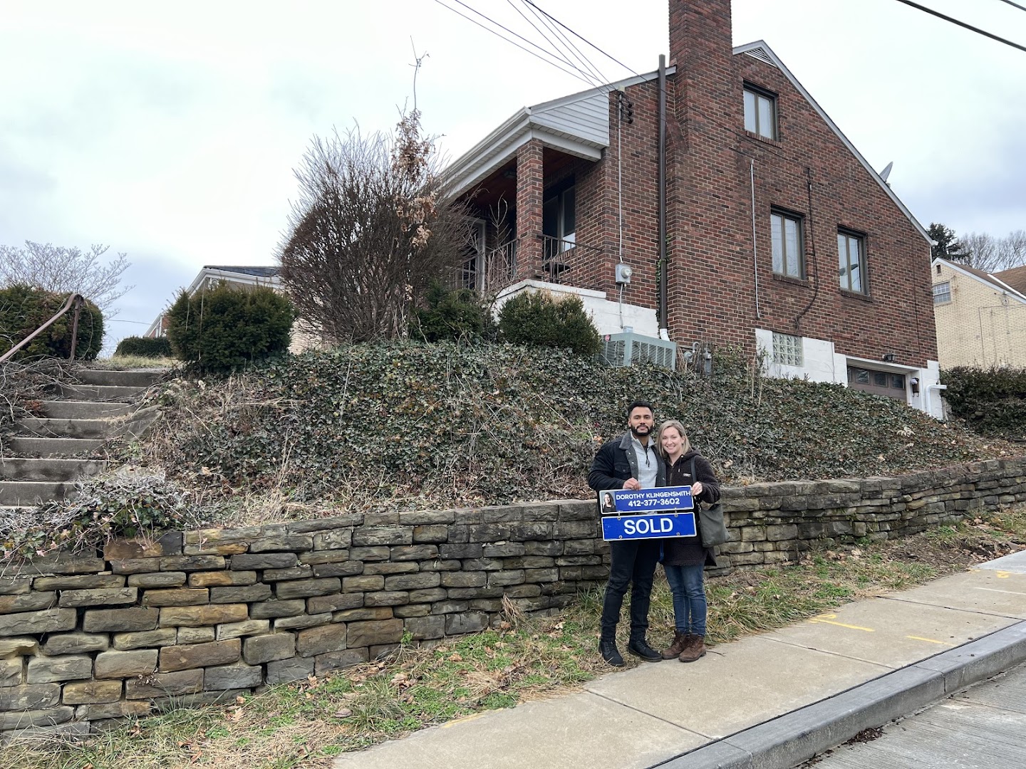 Couple and realtor posing with SOLD sign outside a Pittsburgh area home on a hillside